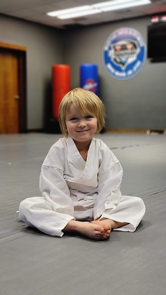 Smiling Lil Dragons student sitting on the mat at Leadership Academy